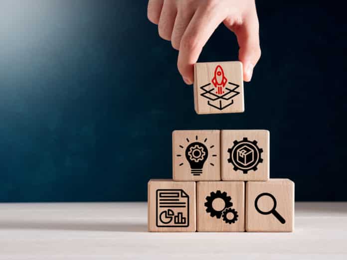 Product development, launching, analysis and market validation. MVP, minimum viable product concept for lean startup. Hand puts wooden cubes with new product launch icons.